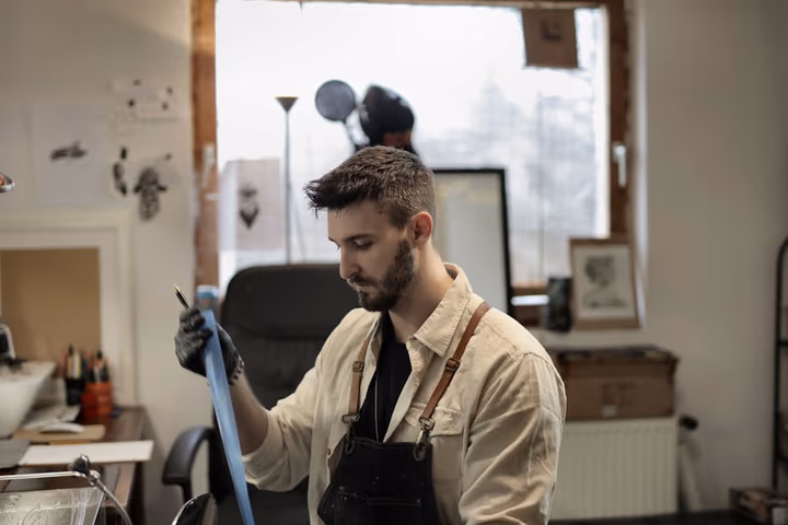 Artisan concentré sur son projet dans un atelier, portant des gants de protection et un tablier.